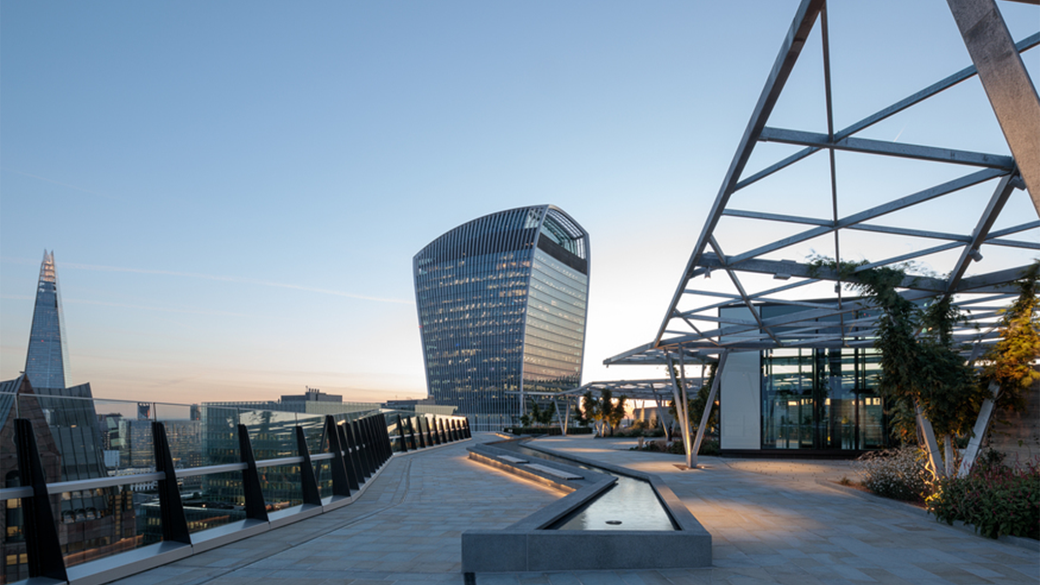 A picture of the Garden at 120 rooftop area at sunset, with the water feature visible and the Walkie Talkie building behind it.